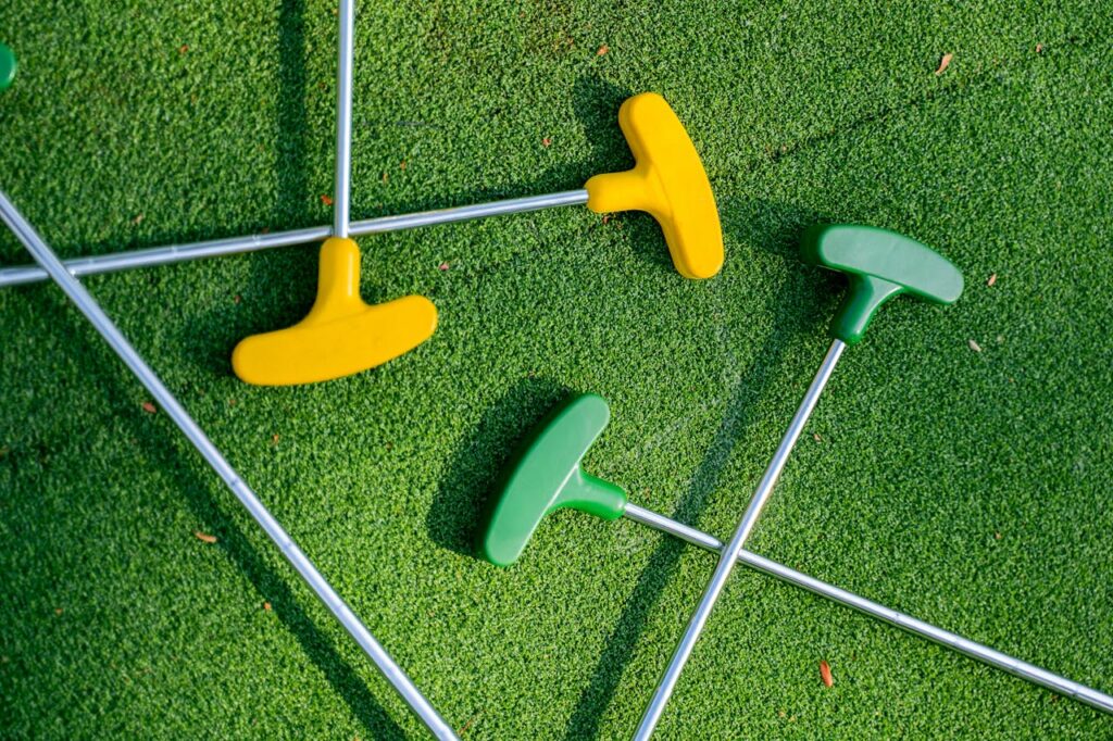 Vibrant yellow and green mini golf putters arranged on a lush green turf, perfect for leisure scenes.