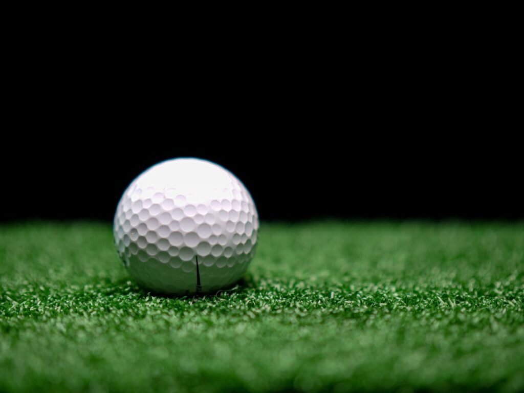 Detailed shot of a dimpled golf ball on artificial turf against a dark background.